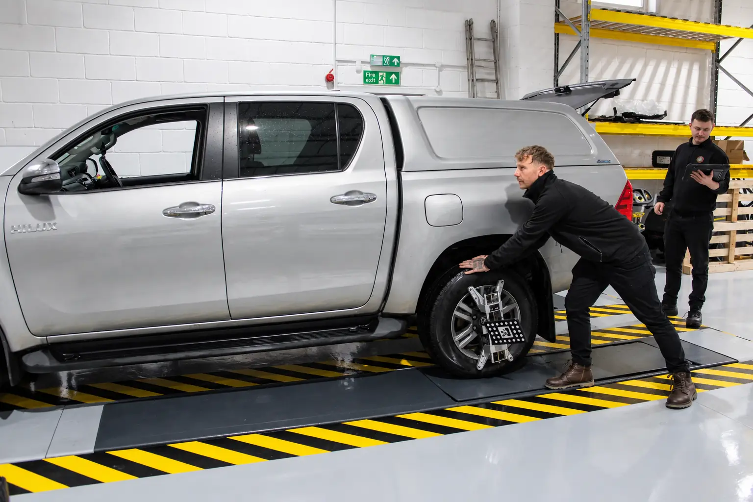 Technicians checking a car's wheel alignment on the ramp