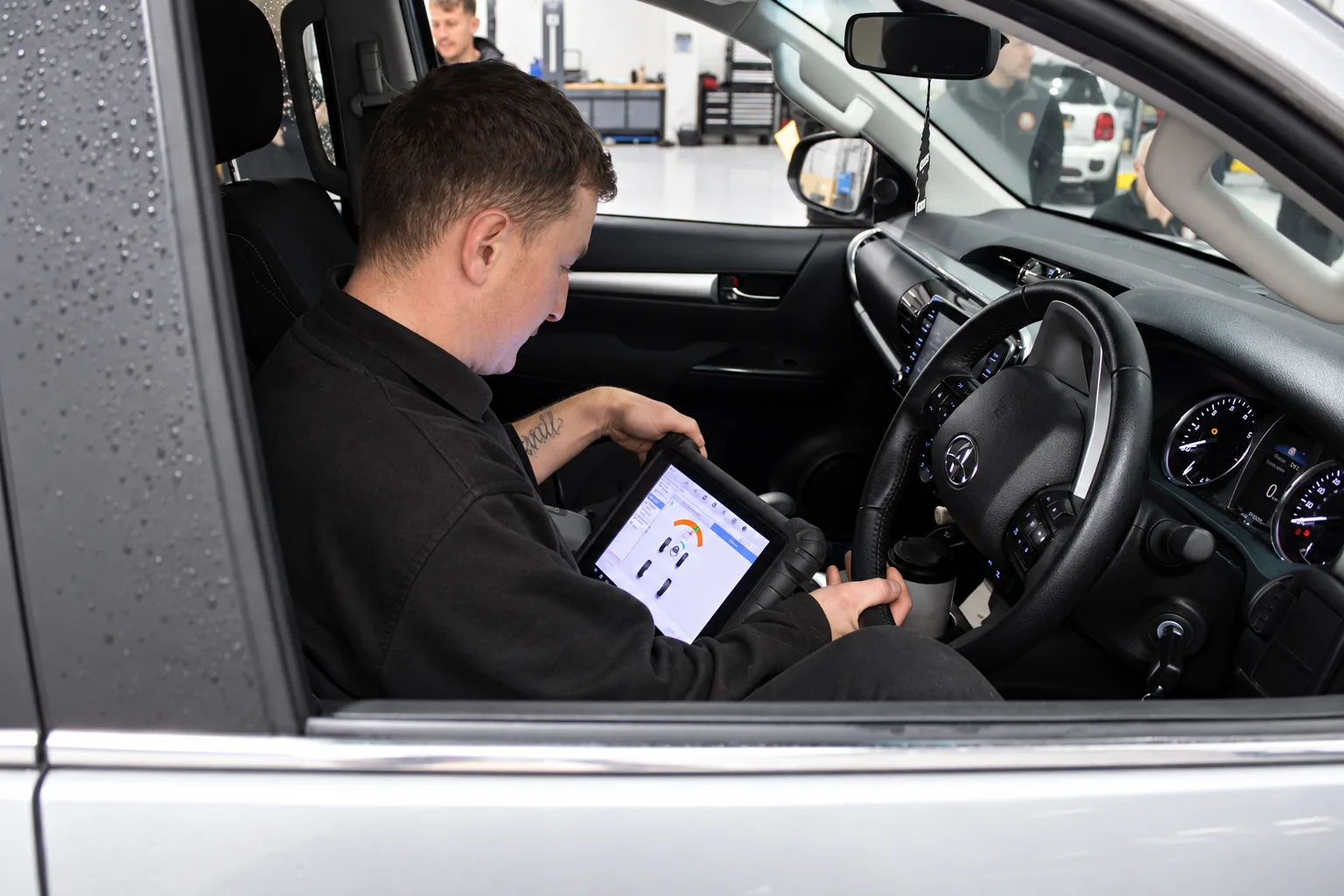 Technician using a tablet inside a car during a wheel alignment check